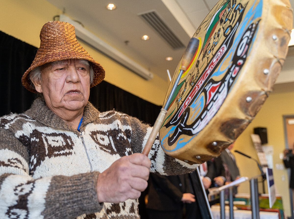 Elder man in traditional garments, drumming.