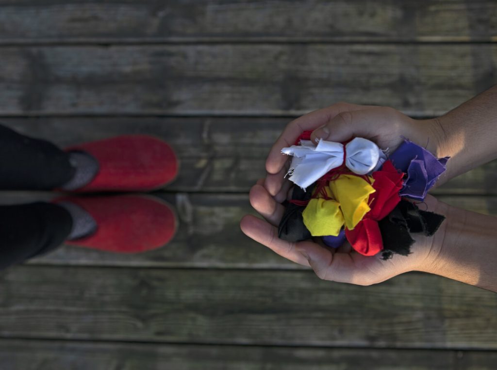 Aerial view of hands holding fabric sachets in different colours, an offering to a person standing across from them.
