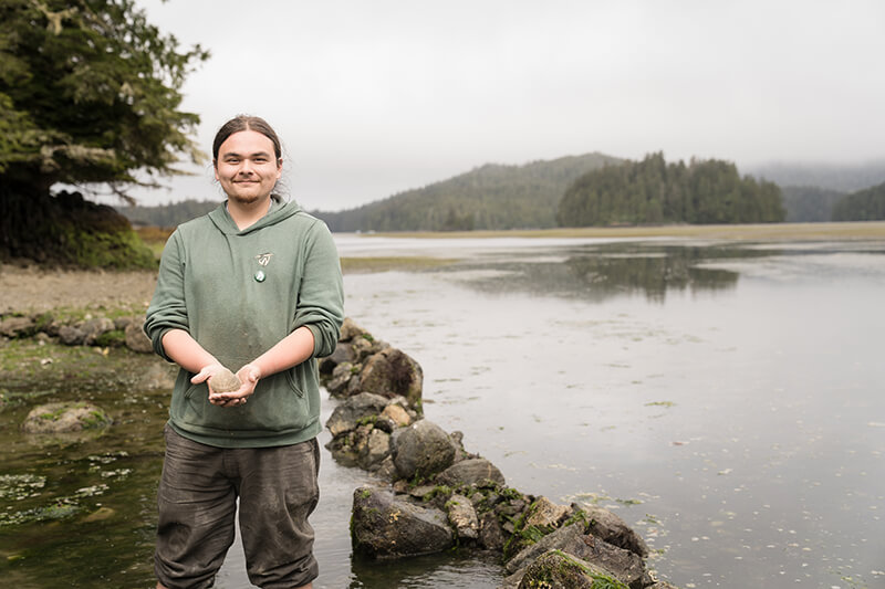 Hughie standing in the clam field holding a clam and smiling at the camera.