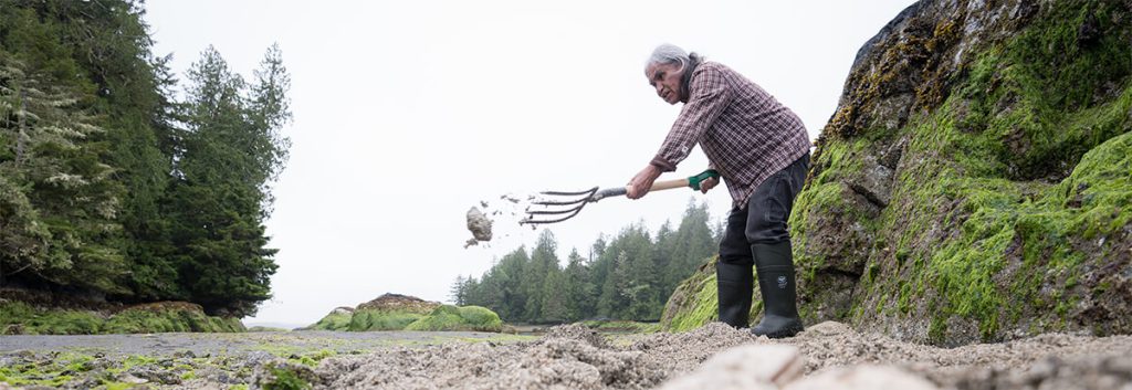 Kyuquot mentor Daniel Blackstone tossing sand with a pitchfork.
