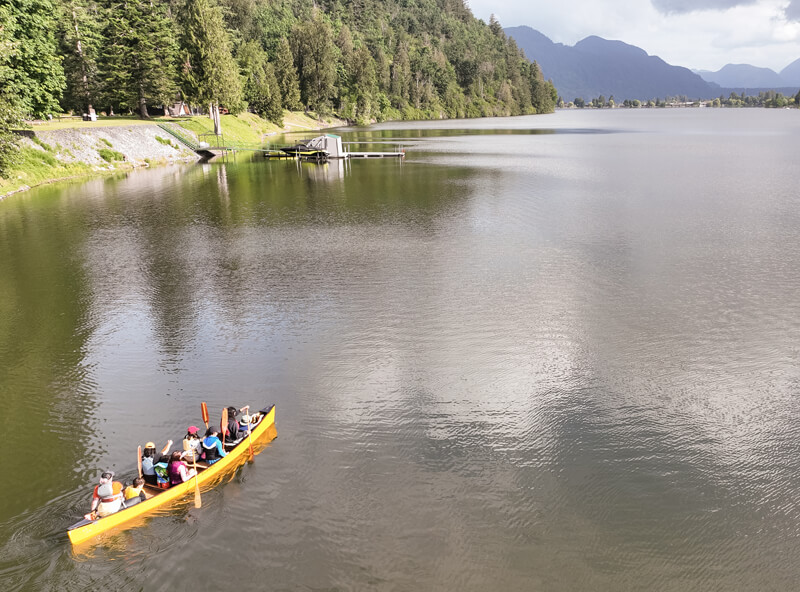 Clara Hunter with her family in a yellow canoe on a lake. Trees and mountain range in background.