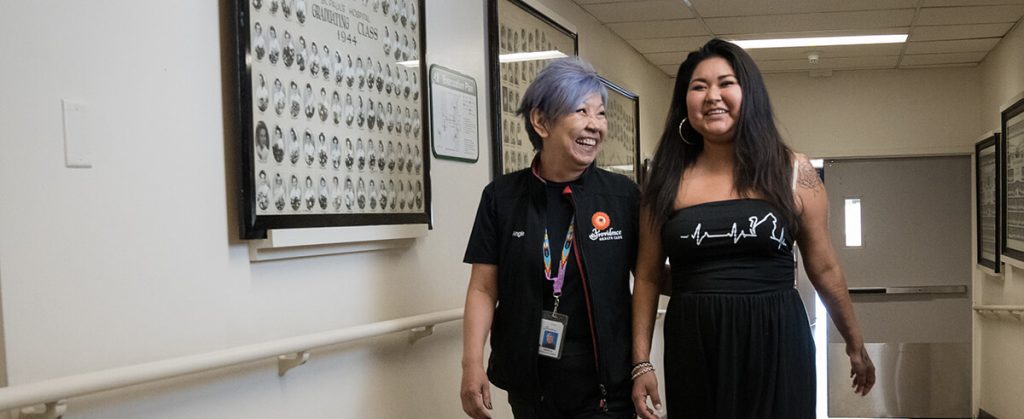 Ange and Raquel smiling and laughing while walking down a hallway.