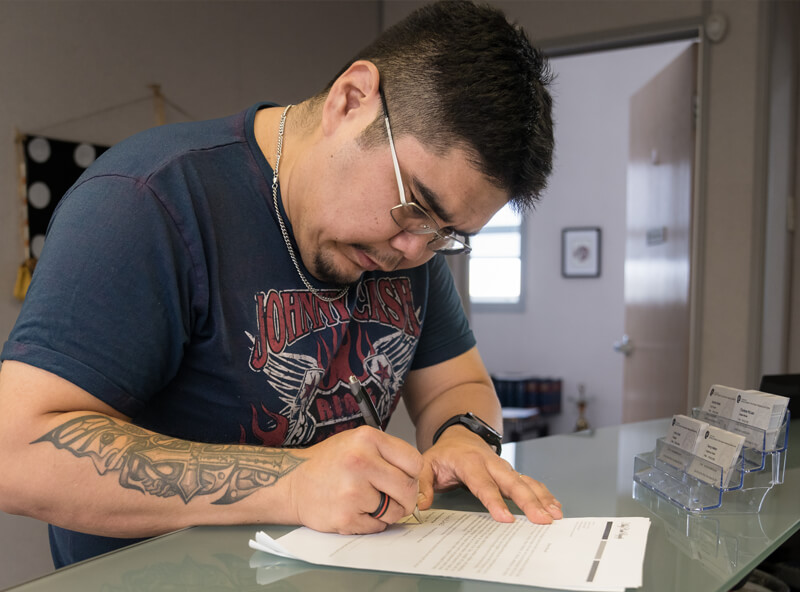 Michael LaRochelle, dressed casually, is seen signing papers at a business' front desk.