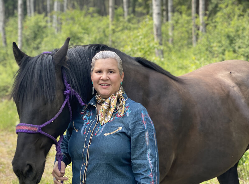 Sunny LeBourdais standing next to a horse, holding a purple woven harness.